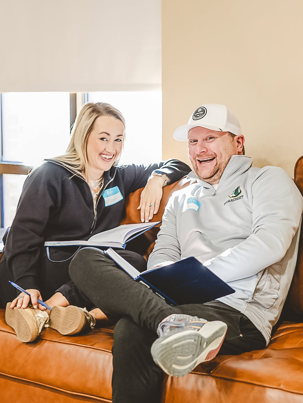 A couple laughing together on a couch with study books